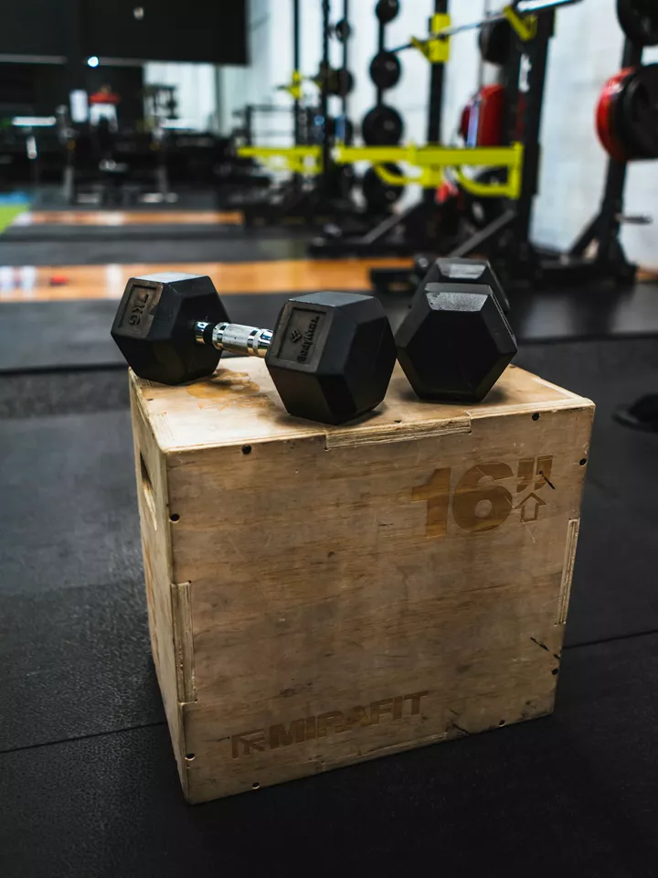 Three dumbbells on a wooden plyo box in a gym